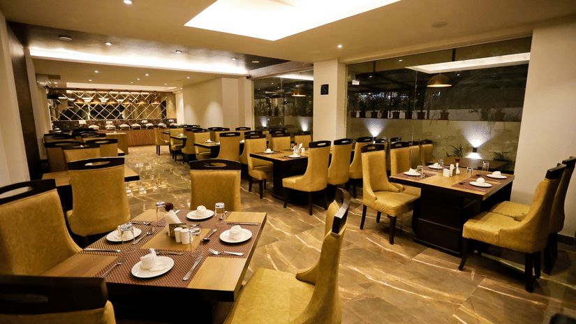 A well-appointed dining area at Amara Grand Baga, Goa, featuring neatly set tables with plates and cutlery, illuminated by soft, warm lighting.